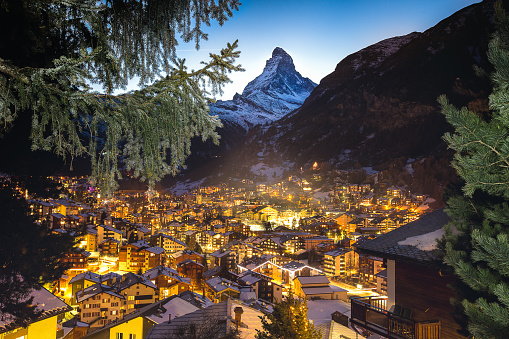 Warm window lights from the swiss alpine village of Zermatt light the valley at twilight with the Matterhorn peak above it