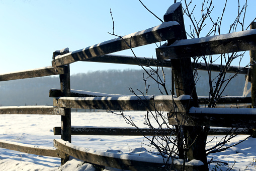 Diminishing perspective of an old wooden fence with frosted snow on its planks, snow covering the mountain under the blue sky