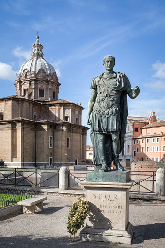 Julius Caesar statue with a wreath at its base and chapel dome and blue sky in the background.  Located near the Roman Forum and Colosseum.  Concepts could include history, leadership, art, and others.