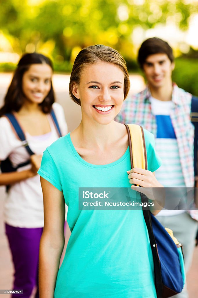 College Girl With Students Standing In Background On Campus Portrait of confident teenage girl with students standing in background on university campus. Vertical shot. 16-17 Years Stock Photo