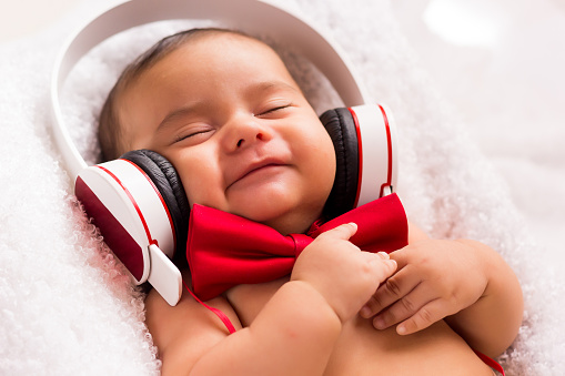 beautiful baby two months old relaxed listening music with headphones, using a vintage red tie and beige pants