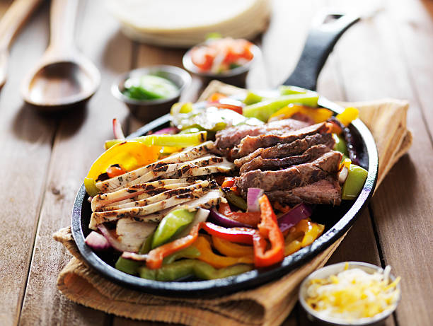 chicken and steak mexican fajitas in iron skillet chicken and steak mexican fajitas in iron skillet shot close up on wooden table fajita photos stock pictures, royalty-free photos & images