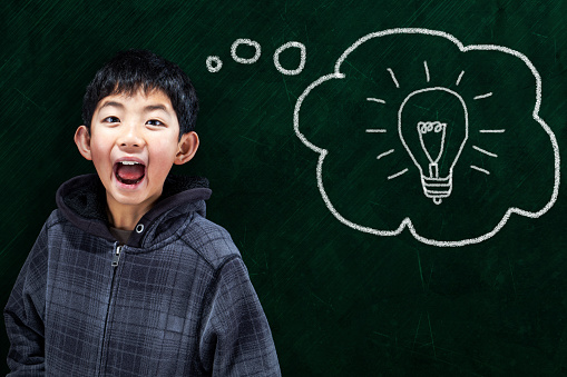 Smart Asian boy with smart idea in classroom setting and chalkboard background.