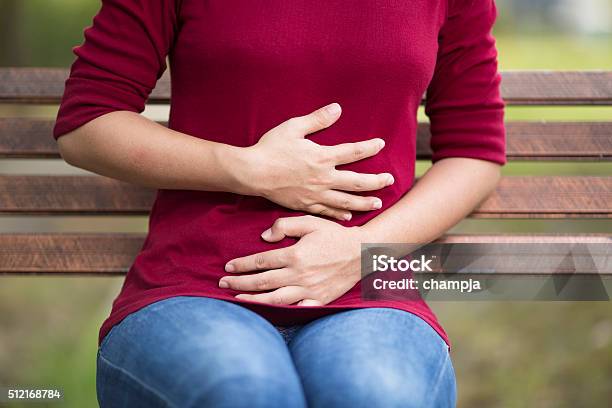 Woman Has Stomach Ache Sitting On Bench At Park Stock Photo - Download Image Now - Abdomen, Stomach, Holding