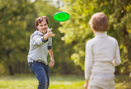 Happy father and his son playing frisbee in the park.  