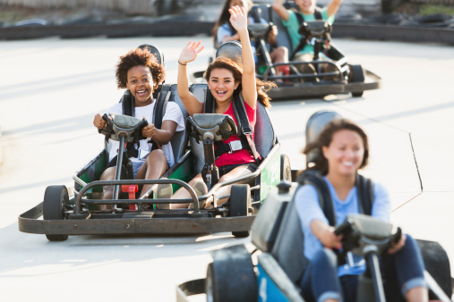 Multi-ethnic teenage girls riding go carts at amusement park.  Focus on two girls in middle (16 years).