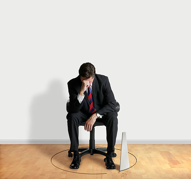 Sabotage A businessman sitting in an office chair with his head in his hands while the floor beneath him is being undercut. sabotage stock pictures, royalty-free photos & images