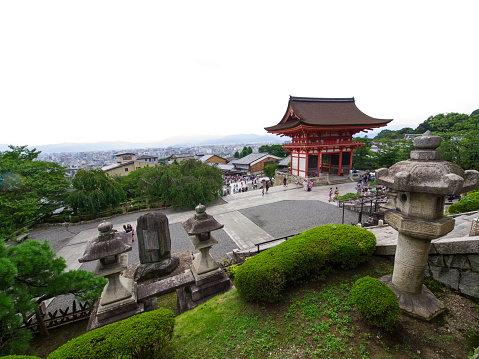 Kyoto, Japan - August 12, 2014: Top view of Kiyomozu Temple grounds. Front is green from grass and bushes, there are some Toros that is traditional lanterns made of stone and a lot of pillar stones with the name of donors to the temple. In background temple entering building and sky as copy space.
