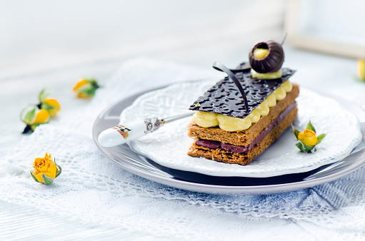 Millefeuille, french pastry with custard and chocolate on a white plate and wooden table