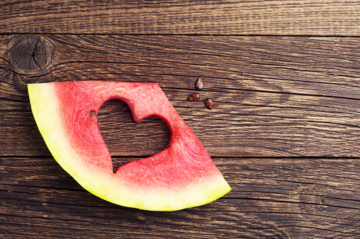Sliced watermelon with cut in the shape of heart on wooden background. Top view