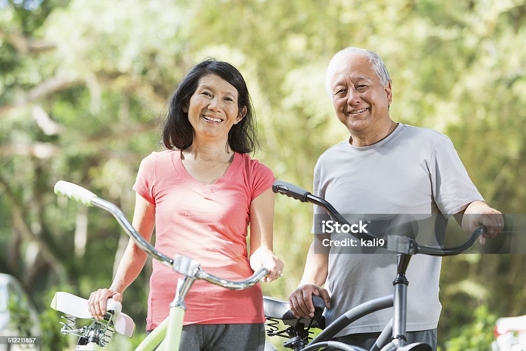 Asian couple riding bicycles Mature Asian couple (60s) in the park, riding bicycles. Asian and Indian Ethnicities Stock Photo