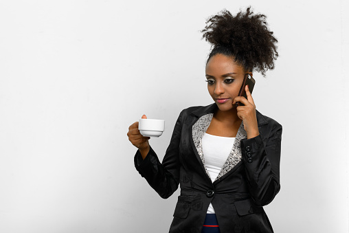 Studio shot of African businesswoman talking on phone and holding coffee cup