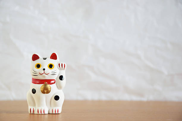 Japanese beckoning cat doll (maneki-neko) Japanese beckoning cat doll (maneki-neko) on wood table and white wrinkled paper background maneki neko stock pictures, royalty-free photos & images