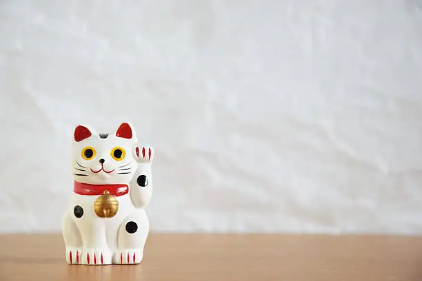 Japanese beckoning cat doll (maneki-neko) on wood table and white wrinkled paper background