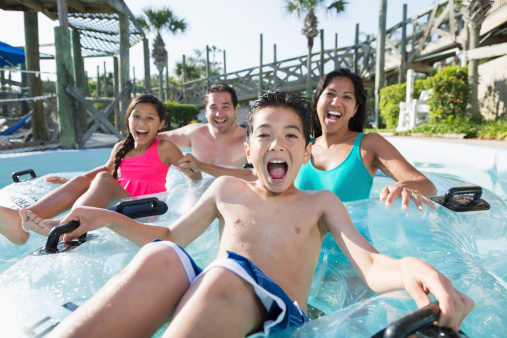 Multi-ethnic family with two children having fun at water park.  Main focus on boy (9 years).