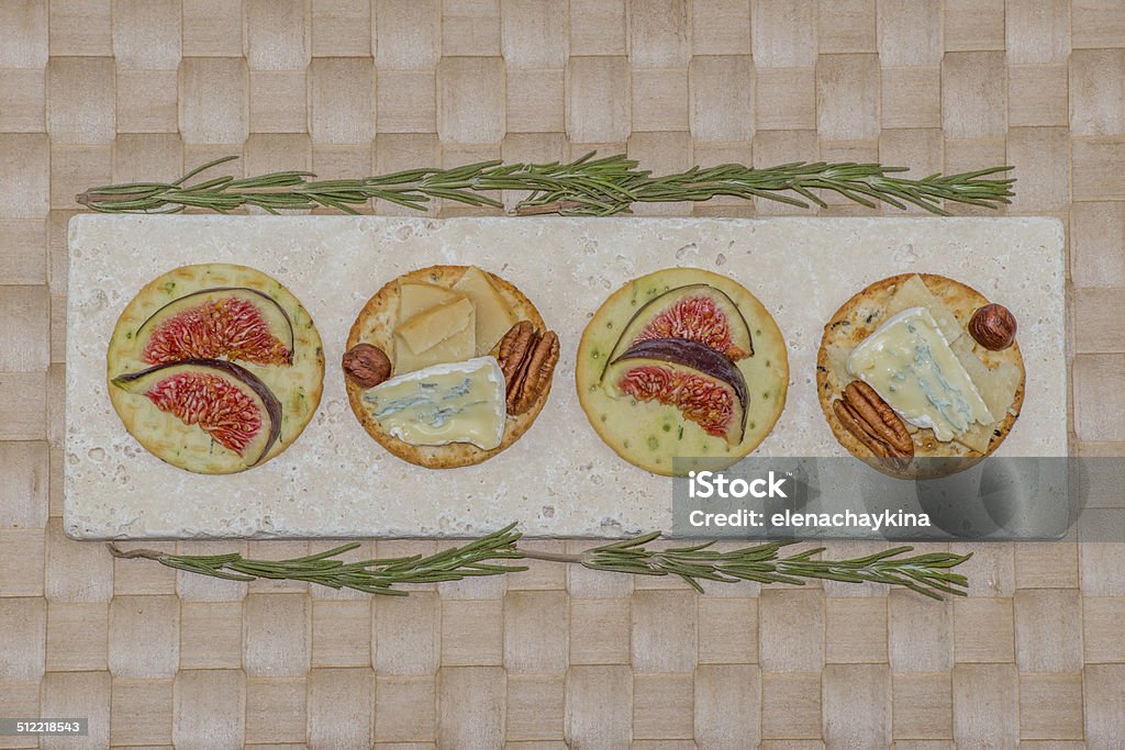 Cheese and figs on crackers on placemat Cheese and figs on four crackers on woven placemat Appetizer Stock Photo