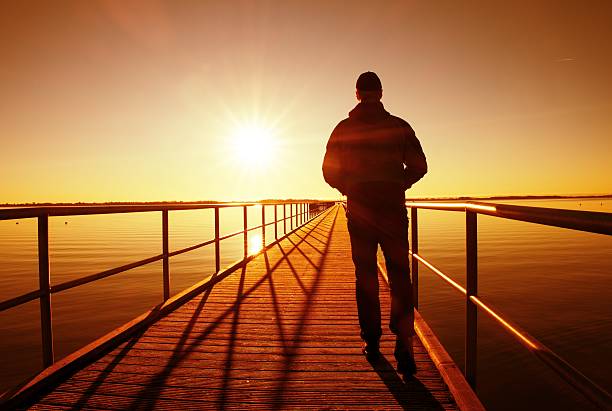 istock Man silhouette walk on wharf construction above sea to Sun 512219306