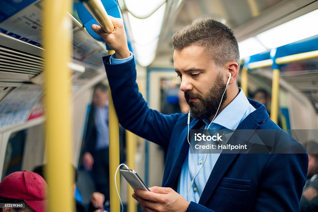 Serious businessman travelling to work. Standing inside undergro Serious businessman with headphones travelling to work. Standing inside underground wagon, holding handhandle. Men Stock Photo