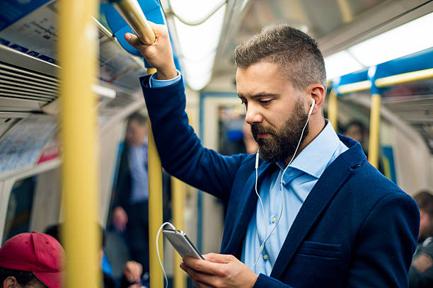 Serious businessman travelling to work. Standing inside undergro Serious businessman with headphones travelling to work. Standing inside underground wagon, holding handhandle. commuter stock pictures, royalty-free photos & images