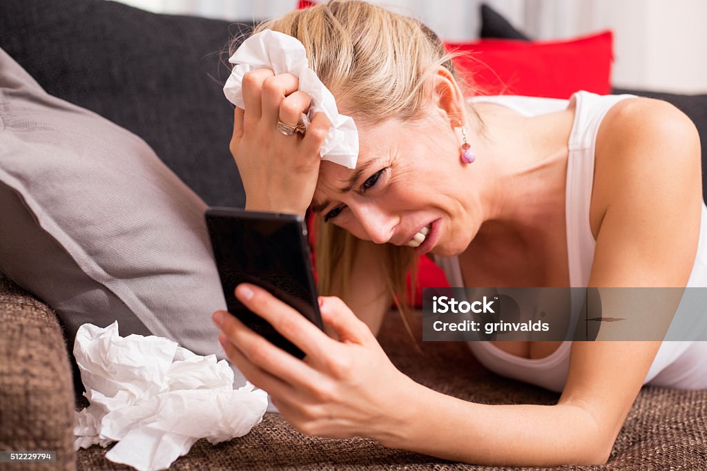 Woman crying on couch with cellphone in her hand Woman crying while lying on couch with cellphone in her hand Depression - Land Feature Stock Photo