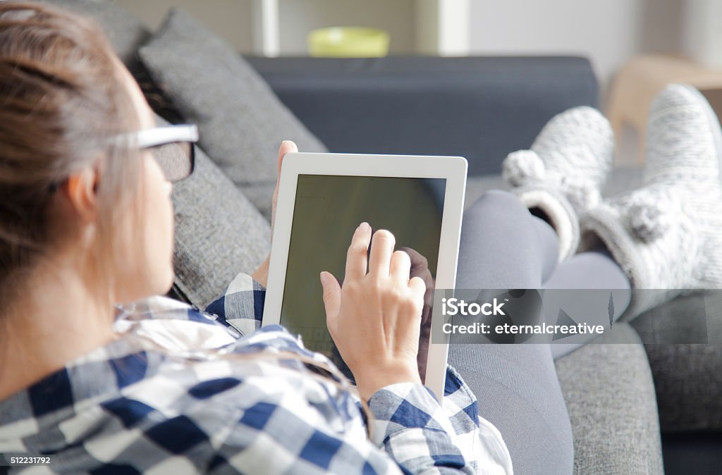 Using tablet Woman lying on sofa in living room and using tablet pc. Digital Tablet Stock Photo