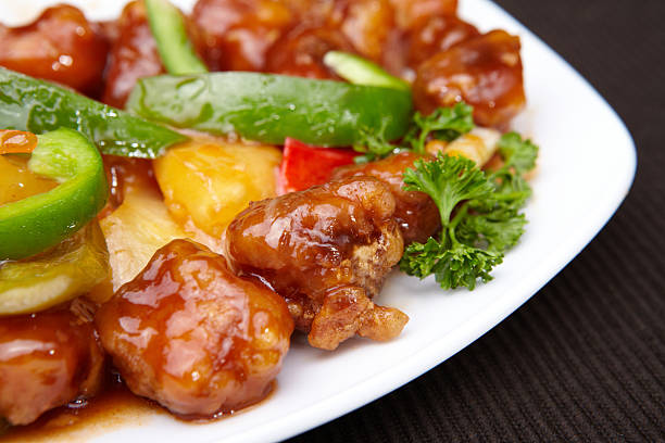 DSLR photo of a Colored Crispy Pork in Tasty Orange Sweet and Sour Sauce with Red, Green and Yellow Bell Peppers Seasoned with Fresh Parsley on a White Oval Plate Photographed in Close-Up from Above with a Large Depth of Field and Arranged on a Black Tablecloth