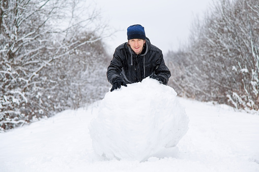 Boy rolls a big snowball to build a snowman in winter day