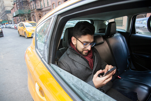 Mixed Race Man looking at his Mobile Phone while sitting in a Taxi Cab in New York City.