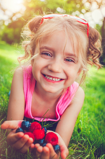 Happy little girl with a handful of berries in summer