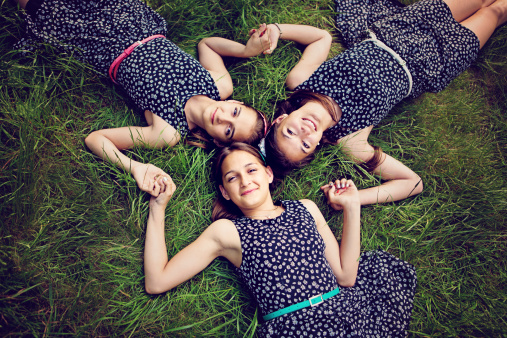 Twin sisters lying in the grass and holding their hands in shape of star