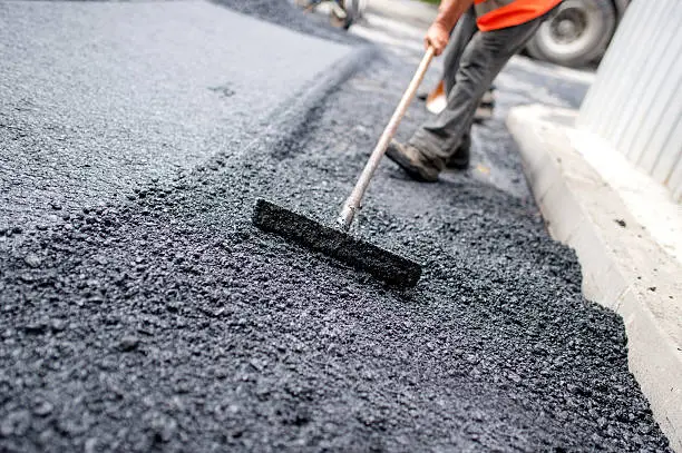 Photo of Worker levelling fresh asphalt on a road construction site