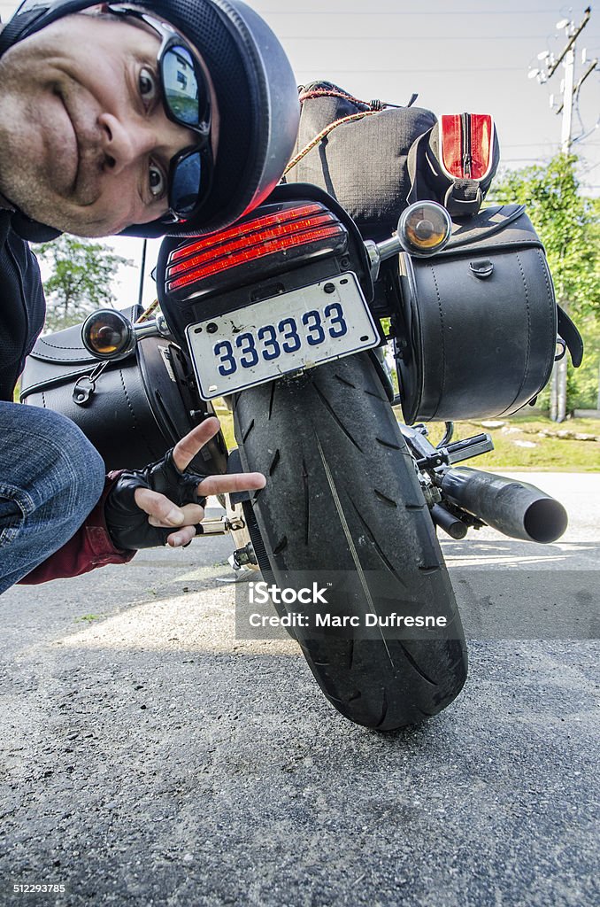 Worn out tire A motorcyclist showing his worn out rear tire on his motorcycle. He shows this is the second time it happens to him. Motorcycle Stock Photo