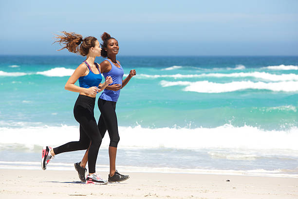 Full length side portrait of two young women running along the beach