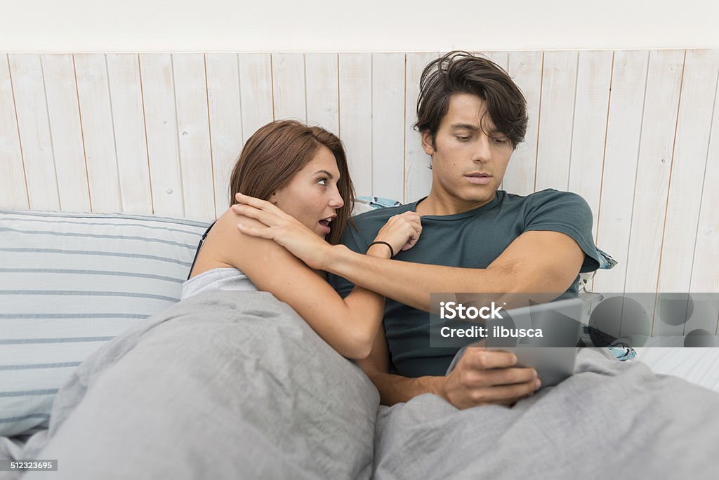 Man rejecting wife to play with his tablet Robber pointing gun against couple in bed Sex and Reproduction Stock Photo