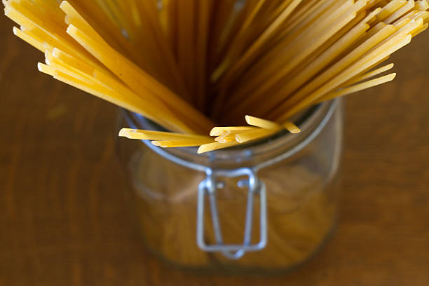Close-up overhead view of a glass jar containing uncooked (sunlit) spaghetti. Some copy space available.