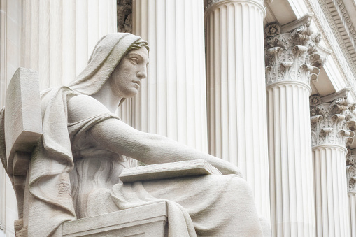 Lady Justice statue sits in front of courthouse columns.