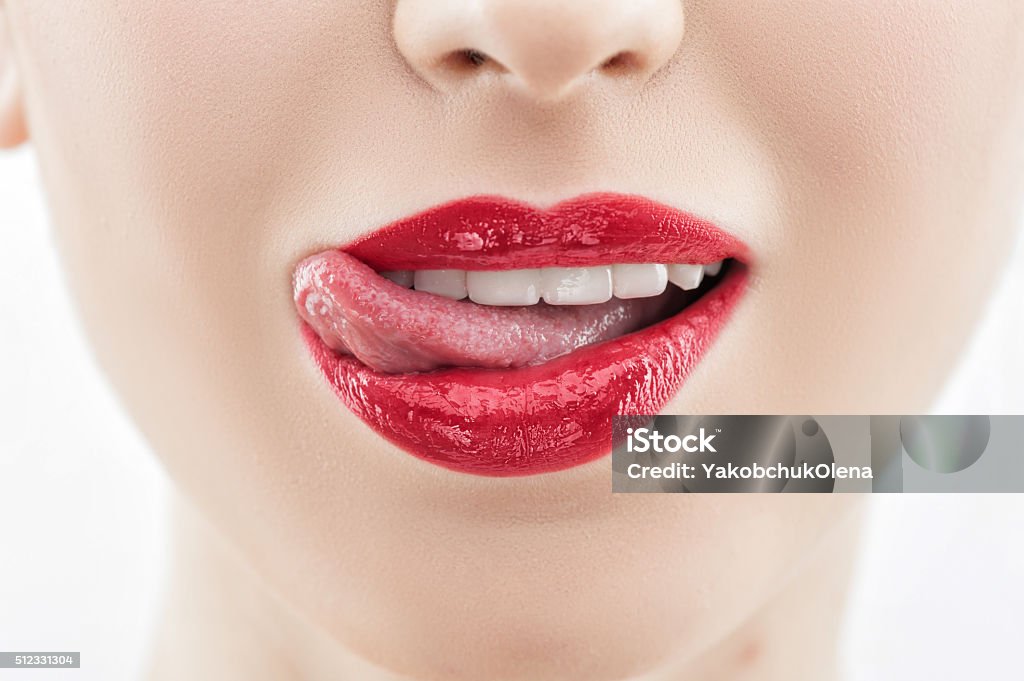 Attractive young girl is evincing her desire Close up of red lips of beautiful woman. She is licking her lips with her tongue. The woman is seducing and smiling with passion Human Lips Stock Photo