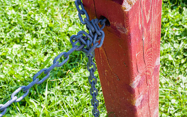 istock Red fence post with tied metal chain against grass 512331528