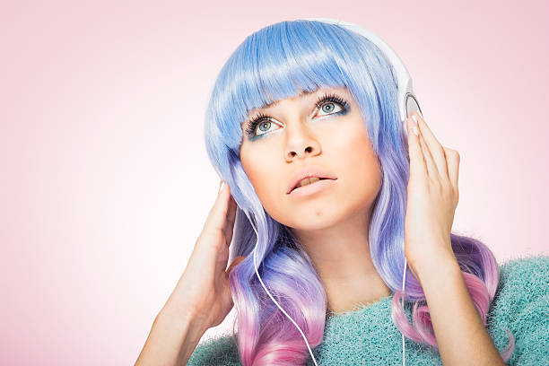 Gorgeous young woman with blue and pink hair and headphones Modern pretty young woman with pastel pink and blue hair and makeup, listening to music on headphones, posing, looking up, wearing pastel green sweater. Pink background, retouched, studio lighting. cosplay photos stock pictures, royalty-free photos & images