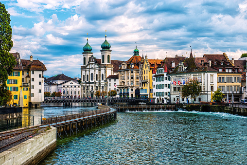 Beautiful Cityscape of old town Lucerne, visible are Jesuit Church, the river Reuss waterfront of Lucerne with the famous Kapellbrucke bridge built in 1333, traditional swiss buildings, restaurants, coffee bars, hotels, beautiful cloudscape and reflection in the water.  