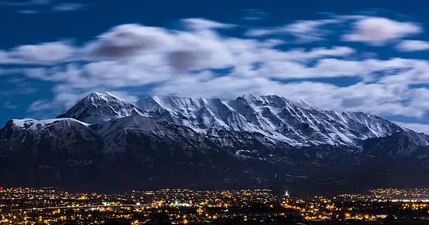 Snow capped Wasatch mountains under a full moon.  Mount Timpanogos can be seen towering over Utah city lights glowing in Lehi, American Fork, Pleasant Grove, and Lindon.  Image captured February 2016.