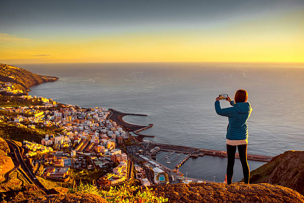 Woman enjoying landscape view near Santa Cruz city Young female traveler in blue jacket photographing Santa Cruz city standing on the top of the mountain on La Palma island in the morning canary photos stock pictures, royalty-free photos & images