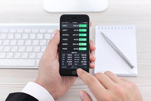 Businessman holding iPhone 6 with application Stocks of Apple Alushta, Russia - November 3, 2014: Businessman holding a iPhone 6 Space Gray with application Stocks of Apple on the screen. iPhone 6 was created and developed by the Apple inc. apple device stock pictures, royalty-free photos & images