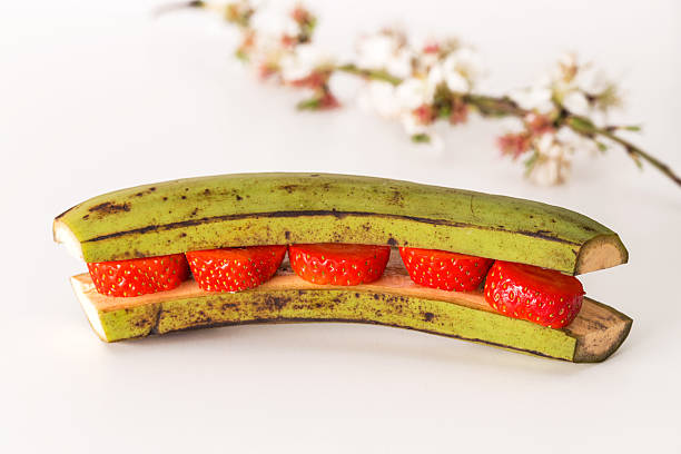 bananas stuffed with cream and strawberries with mint on white background