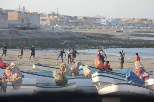 Sur, Oman, October 22, 2013: playing football on the nbeach in Oman. A group of omani bouys playing football on the beach, trough fishing boat, facing the sea