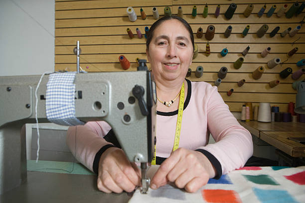 Woman Using Sewing Machine In Laundry Portrait of smiling middle aged woman using a sewing machine in laundry woman tailor stock pictures, royalty-free photos & images