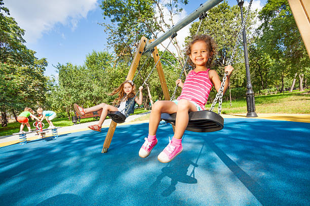 Kids swing on playground Two beautiful little girls swinging on swings on playground with smile on sunny summer day swing play equipment stock pictures, royalty-free photos & images