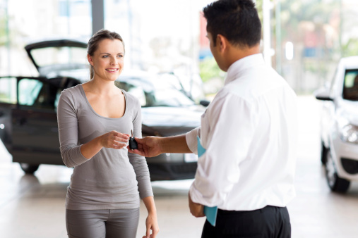 young woman receiving her new car key from salesman
