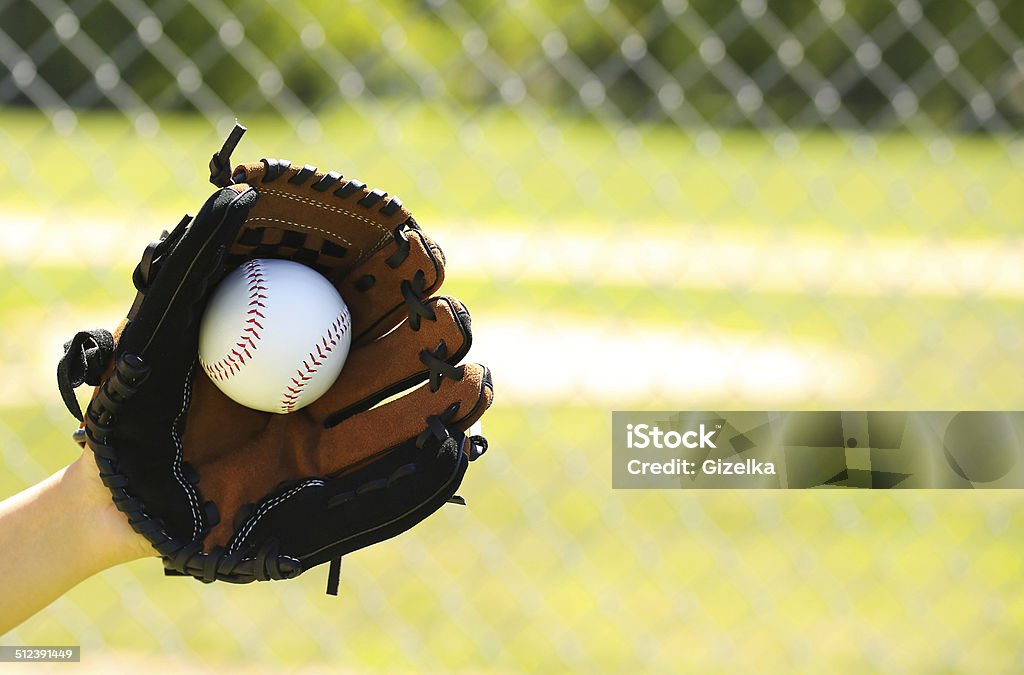 Hand of Baseball Player with Glove and Ball over Field Hand of Baseball Player with Glove and Ball over Field and Net Youth Baseball Stock Photo