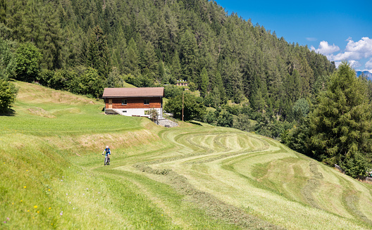 A female mountainbiker is riding on a grass covered foot path through the scenic landscape nearby the village of Lenzerheide at Graubünden Canton, Switzerland.